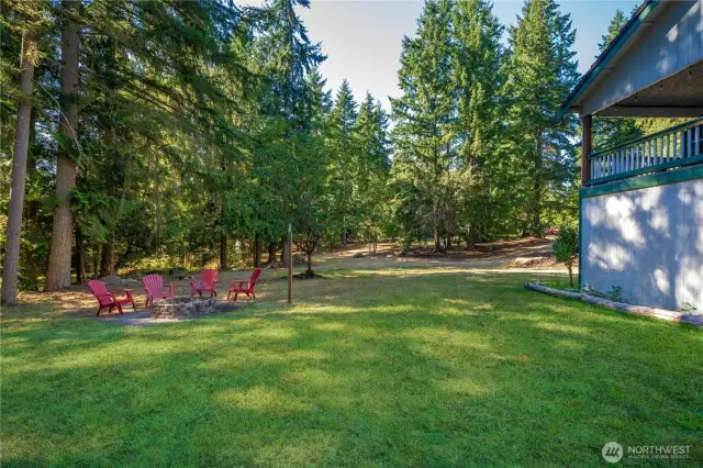 Expansive yard with a cozy firepit seating area surrounded by mature evergreens, offering the perfect spot for gatherings under the stars.
