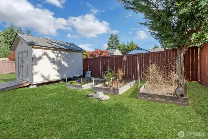 Fenced yard with storage shed and raised garden beds