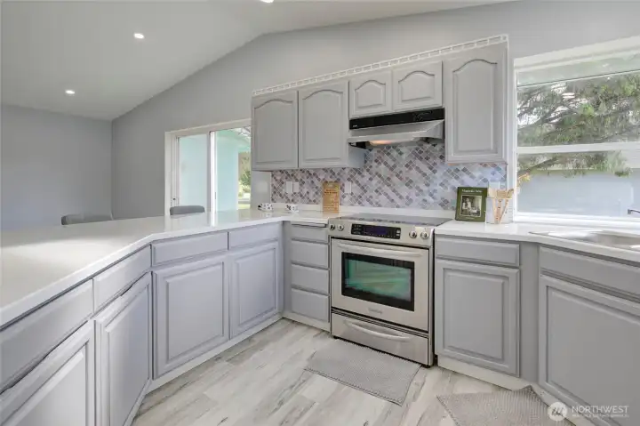 Light-filled, updated kitchen with modern finishes, generous counter space, ample cabinets, stainless steel appliances, and a a cheerful backsplash.