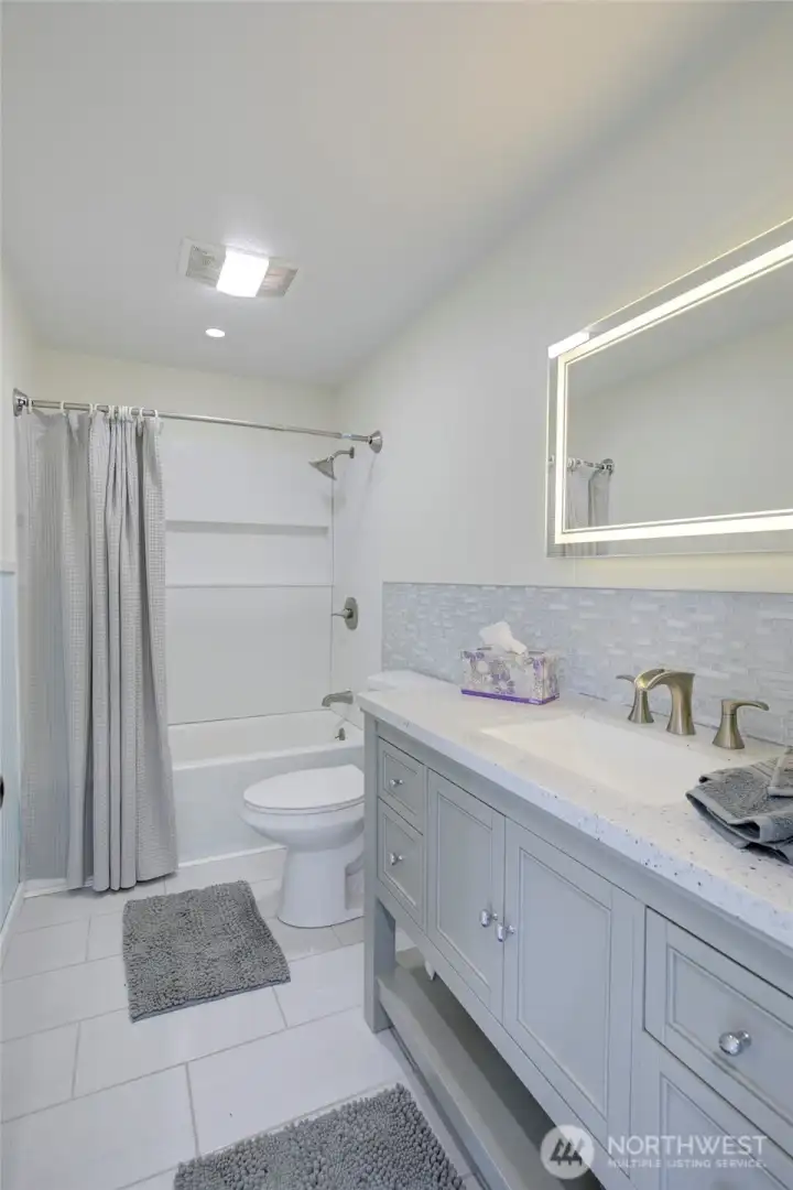 Main floor guest bathroom featuring updated finishes, LED backlit mirror, shower/tub combo, with clean lines and a fresh, modern feel