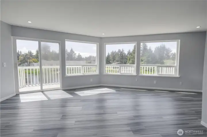 Upstairs bonus area is flooded with natural light through a wall of oversized windows and a sliding glass door that opens to a private balcony, offering treetop views and endless possibilities — perfect for a second living area, home office, playroom, or entertainment space, all with sleek dark hardwood flooring and recessed lighting.