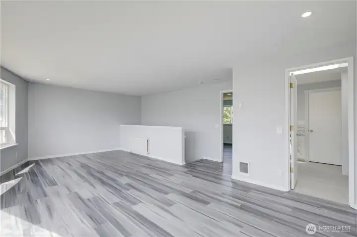 Upstairs bonus area is flooded with natural light through a wall of oversized windows and a sliding glass door that opens to a private balcony, offering treetop views and endless possibilities — perfect for a second living area, home office, playroom, or entertainment space, all with sleek dark hardwood flooring and recessed lighting.