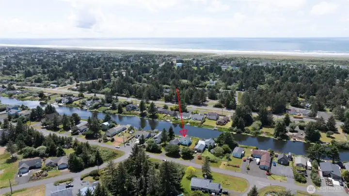 This stunning aerial view showcases the property's unbeatable location — tucked along a peaceful canal with direct water access, all just a short stroll from the Pacific Ocean beach, surrounded by towering evergreens and the natural beauty of the Washington coast.