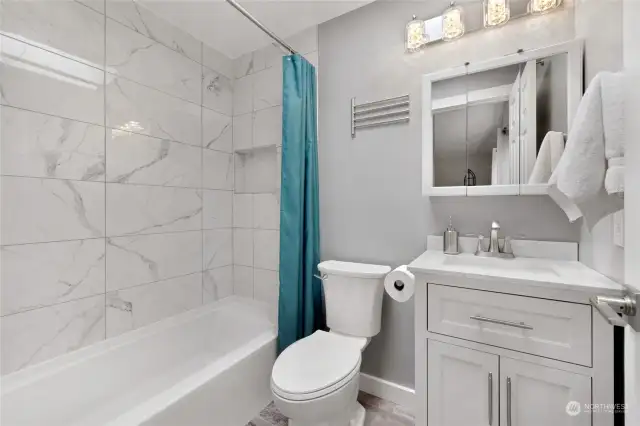 Primary bathroom with new vanity, mirror, lighting, flooring, toilet, and porcelain tiled shower/new shower fixtures.
