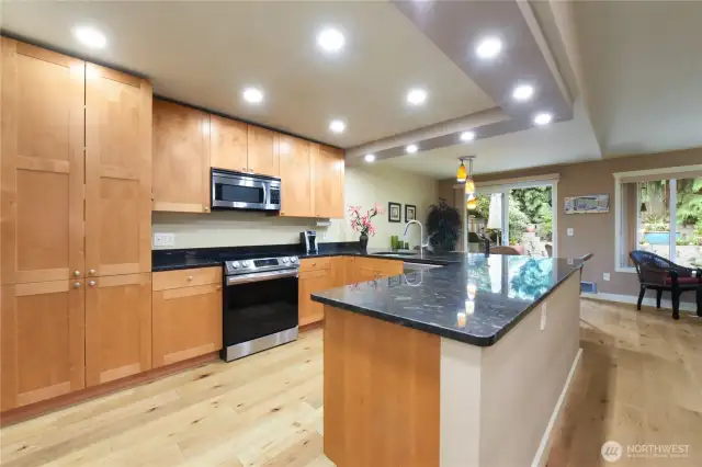 The kitchen features sleek black granite countertops, warm wood cabinetry, and high-end stainless steel appliances, including a built-in microwave, double-door refrigerator and a generous breakfast bar