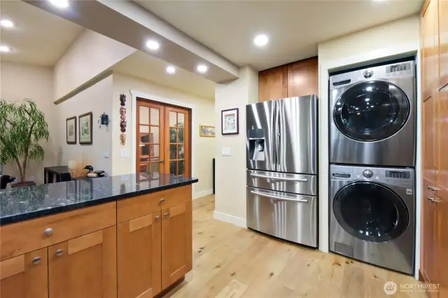 This thoughtfully designed space combines kitchen convenience with smart utility integration. Featuring sleek stainless steel appliances, including a French-door refrigerator and stacked LG washer and dryer