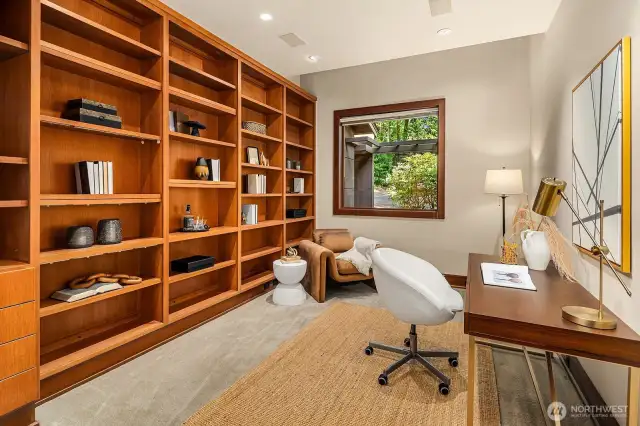 The office, with custom built-ins, overlooks the beautifully landscaped front courtyard and entryway, framed by mature, blooming rhododendrons and lush greenery.