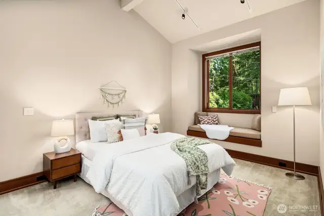 Bedroom #4 features a vaulted ceiling and a south-facing window that fills the room with light, offering peaceful privacy and views of the quiet end of the lane where the home is tucked away.