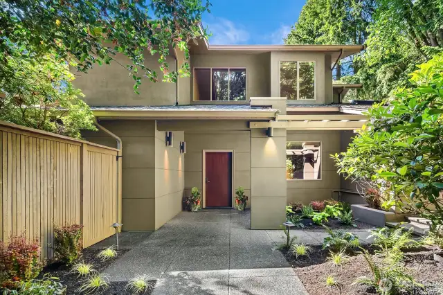Lined with lush landscaping and shaded by mature trees, the elegant front walkway offers a warm welcome with dappled natural light.