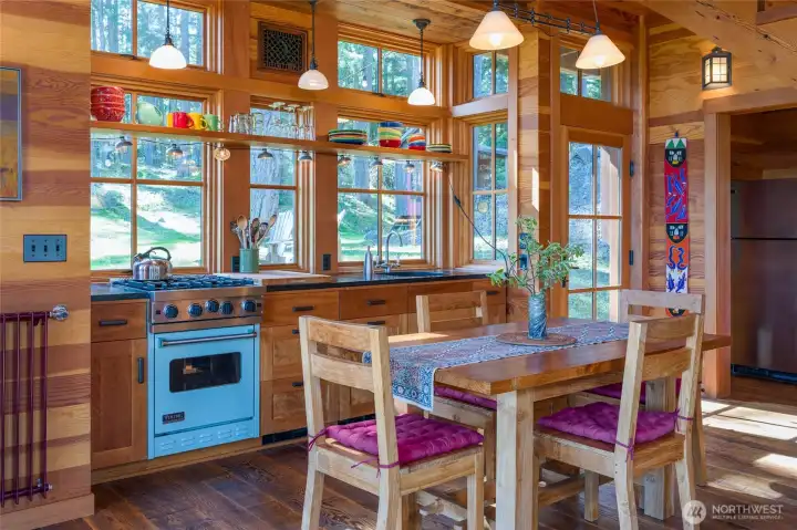 Functional kitchen space with wood framed windows, soapstone counters, floating shelves, and Viking gas range.