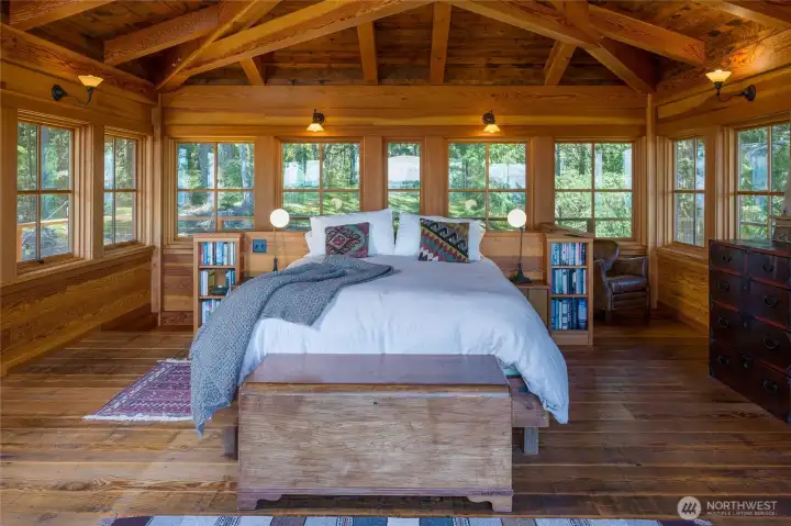 Vaulted ceilings with heavy timber frame beams and walls of windows offer a stunning setting for the primary bedroom