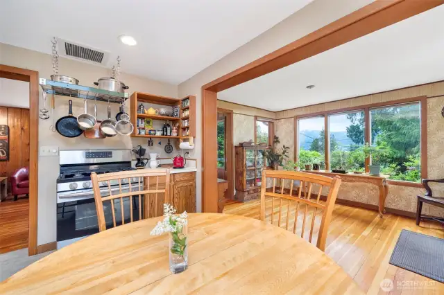 Looking across the dining table toward the gas range and spice cabinet with the entry room to the right and the living room beyond.