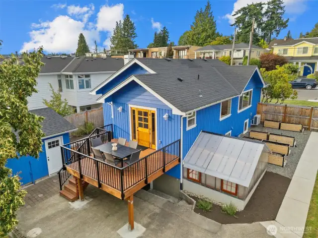 An ideal outdoor living space with a generous deck, lush lawn, greenhouse, garden beds, and room to relax or play.