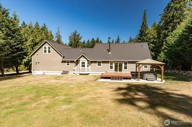 Back of house with automatic generator on the left and gazebo covered hot tub and deck