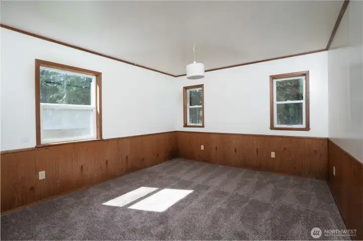 Spacious bedroom with multiple windows bringing in natural light and views of the surrounding greenery. Neutral tones and ample space offer flexibility for a variety of furniture layouts.