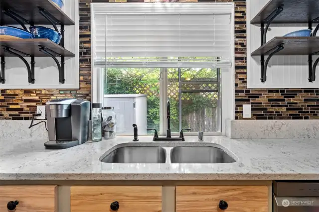 Granite slab counters with matching side splash adjoining glass tile back splash that wraps the window above under mounted double stainless steel sink.