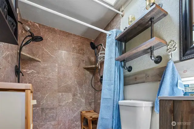 Dual shower heads in tile shower. Industrial wall mount pipe shelving. Skylight above with adjustable blinds.