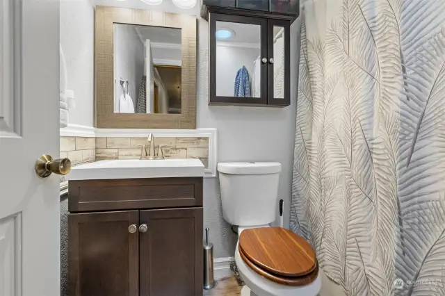 Full guest bathroom with shower/tub combo. Trim wraps the tile back splash above vanity with storage space. Medicine cabinet with additional mirror above potty.