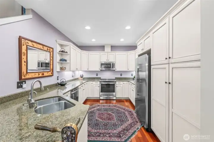 The lovely white cabinetry of the kitchen with newer appliances, granite countertops, and under-cabinet lighting.
