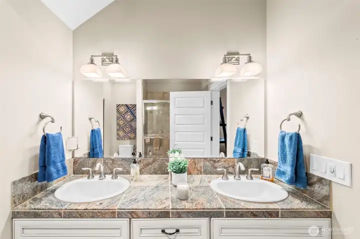 Dual vanity of the Primary en suite bathroom, and a fully tiled walk-in shower with sliding doors.