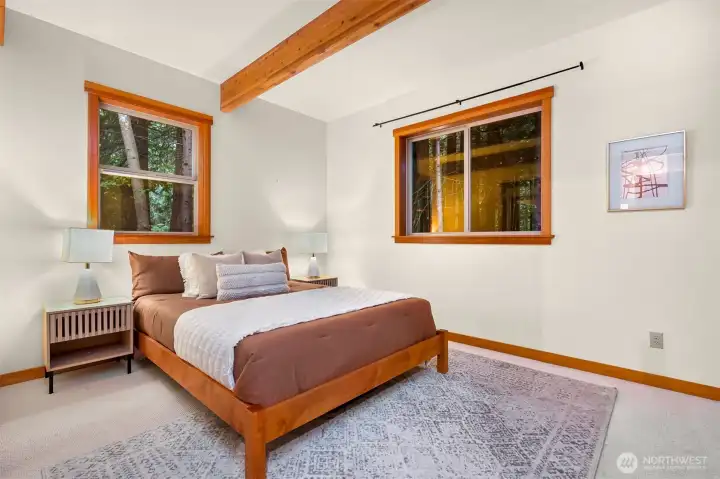 Wake up to peaceful forest views in the spacious second bedroom, where exposed beams and large windows create a warm Pacific Northwest retreat.