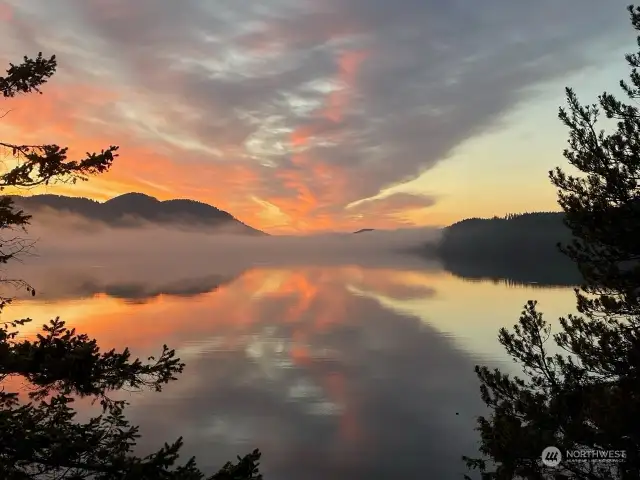 Warm golden hues reflect off the clouds and water as the sun rises over the mountain