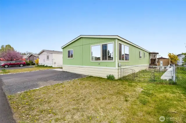 Grassy front yard and gravel drive next to the paved parking. Three parking spaces.