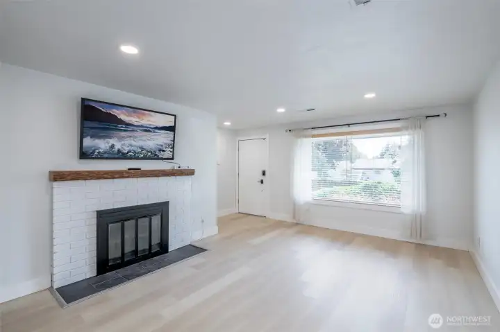 Living room.  Main entry is at the far end of this photo to the left of the large window.  Wood Fireplace.  55" Samsung TV conveys with sale.