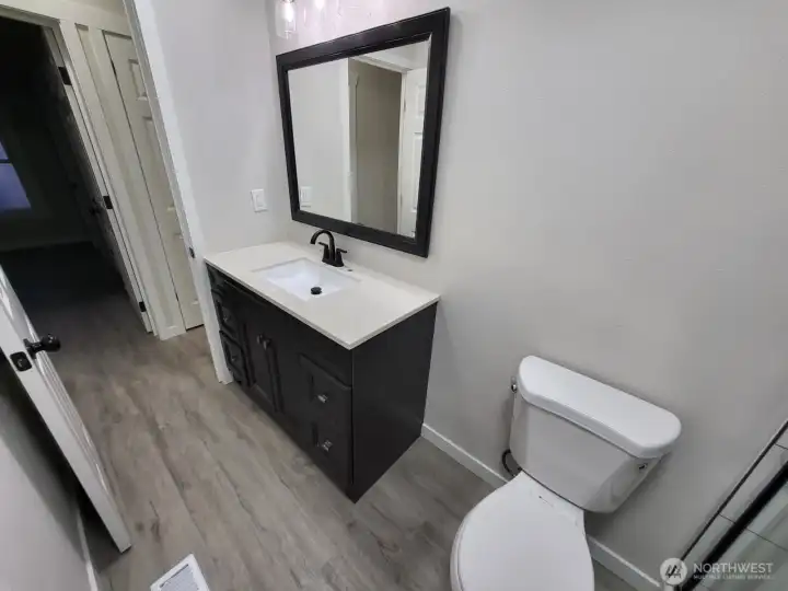 View of the vanity (and hallway) from the shower (dark room across is bedroom #2 we just saw). We are going to exit the bathroom and take a left, and immediately on our left will be bedroom #3.