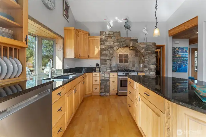 View 2 of kitchen w/ hardwood floors, stainless steel appliances, quartz countertops, wood beams, walk-in pantry, adjacent utility room and stone surround stove and oven.