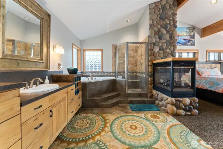 View of main level Primary Bedroom bathroom suite w/ stone fireplace, quartz countertops and soaking tub.