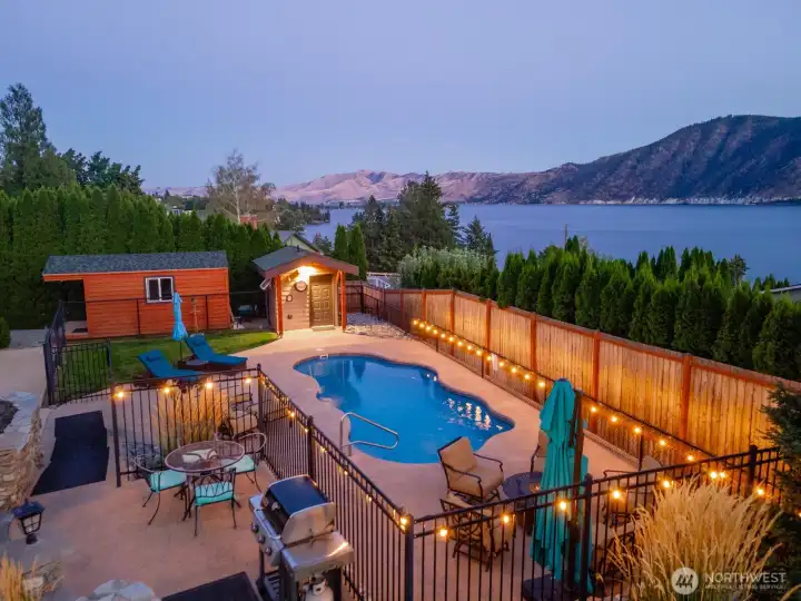 Twilight view of outdoor living area w/ pool, hot tub, basketball court, landscaped grounds and dining and lounge areas overlooking Lake Chelan.