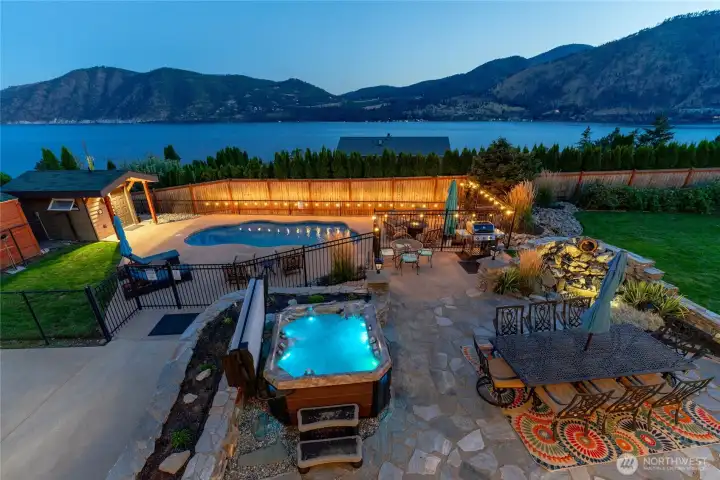 Twilight view of outdoor living area w/ pool, hot tub, basketball court, dining and lounge areas, landscaped grounds and water feature overlooking Lake Chelan.