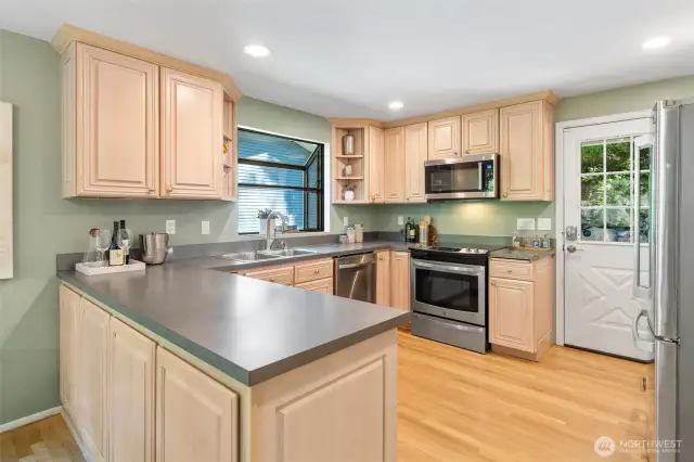 This well-appointed kitchen features a smart, functional layout with ample counter space, stainless steel appliances, and a charming garden window over the sink. A convenient door opens directly to the front patio, creating a seamless indoor-outdoor connection perfect for everyday living and entertaining.