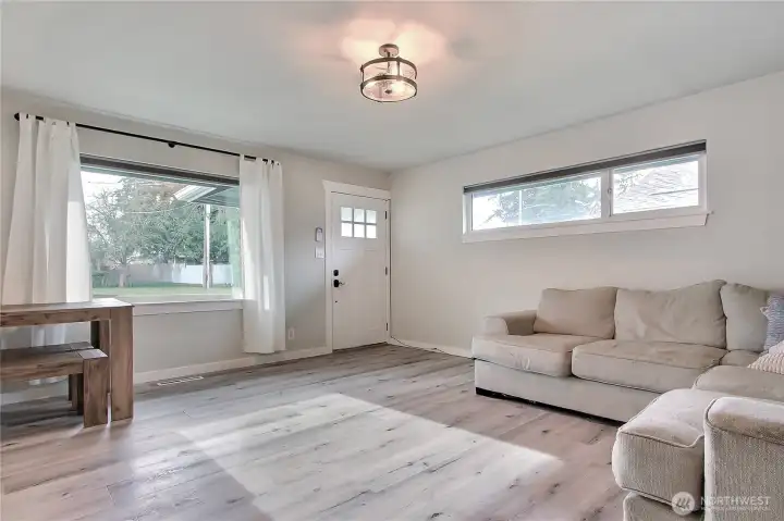 Bright living room with LVP flooring, updated lighting, and large windows for natural light.