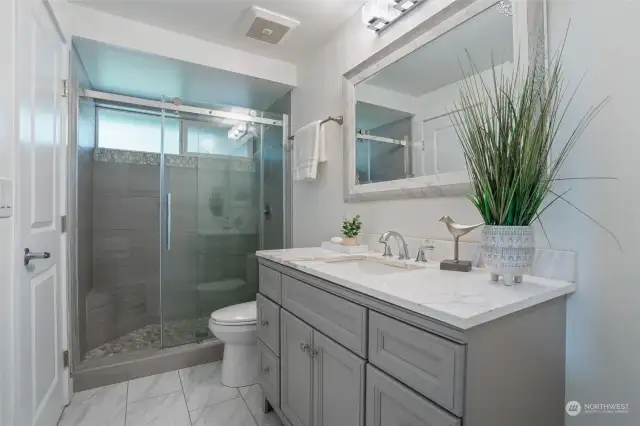 A spa-like main guest bath enjoys an upgraded vanity, new marble tile flooring, fixtures, lighting and gorgeous walk-in shower.