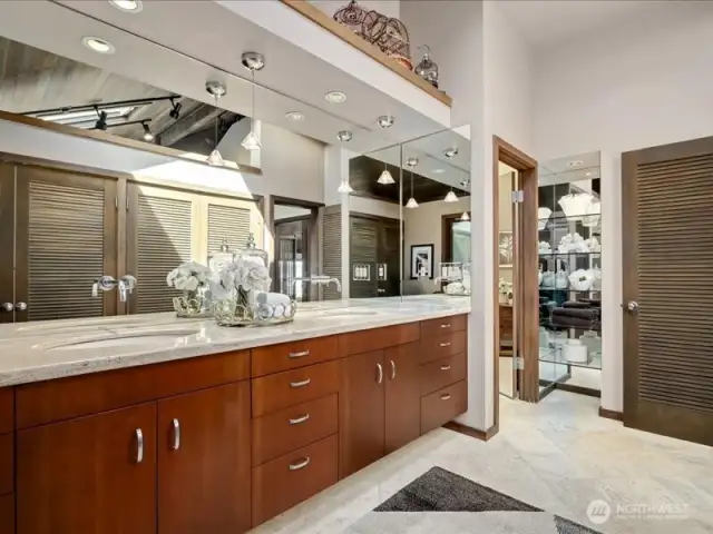 The luxurious Primary bath boasts double sinks in slab travertine countertops and floors, elegant lighted glass shelves, and a separate shower and commode area for added privacy.