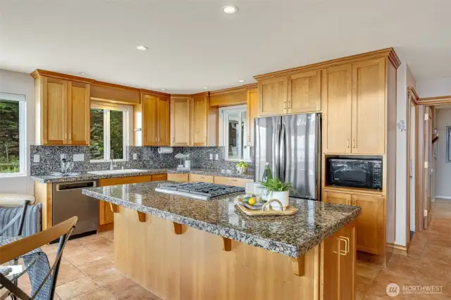 The kitchen is the main hub and features granite tile countertops, stainless appliances, a gas/propane cooktop, ample counter space, including an island and cabinetry.