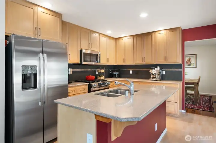Kitchen with quartz countertops, island with sink and gas range and shaker style cabinetry.