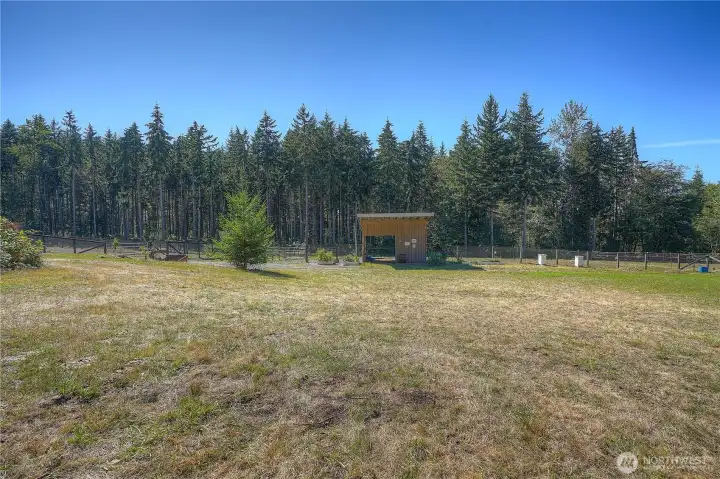 View of the 18 x 18 x 10 stick built loafing shed with overhang - perfect for hay storage or sitting area. Paddocks, and wooded trails are beyond.
