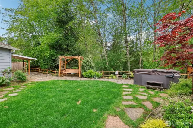Back yard showing off hot tub, bench seating, and privacy from green space.