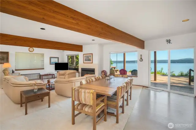 Open floor plan showcases breathtaking views of Hood Canal and the Olympic Mountains, with sliding doors that lead seamlessly to the spacious deck for indoor-outdoor living. The entry hall and stairs to the upper floor are behind you in this photo.