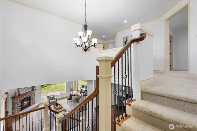 Grand staircase with elegant wrought iron railing and a striking chandelier, overlooking the sunlit great room below.