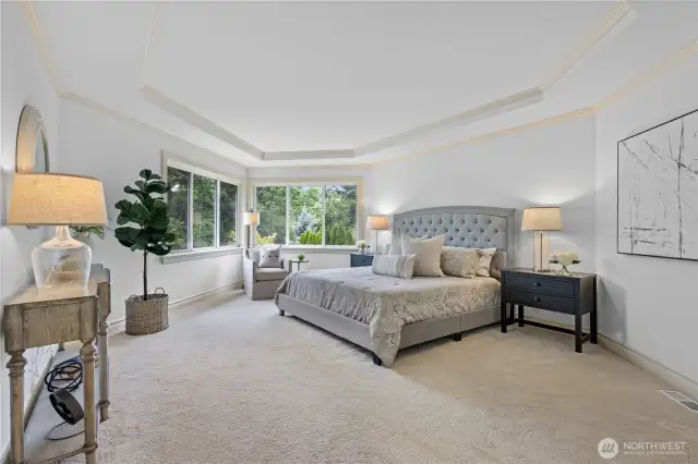 Serene primary suite with tray ceiling and peaceful greenbelt views.