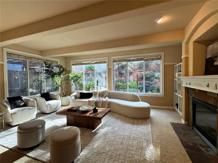 A sophisticated living space wrapped in natural light, with picture windows framing lush landscaping and curated designer staging. Comfort meets elegance in a room created for both connection and calm.
