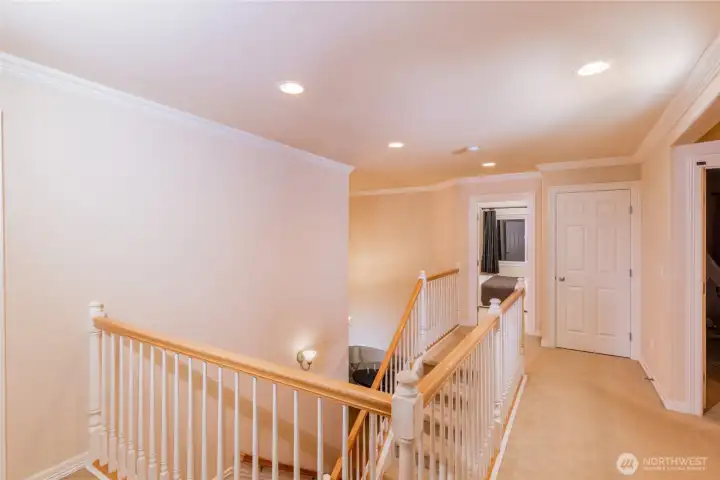 A wide, airy upper landing with crown molding, recessed lighting, and an open balustrade overlooking the entry. This transitional space enhances the home’s sense of openness and flow.