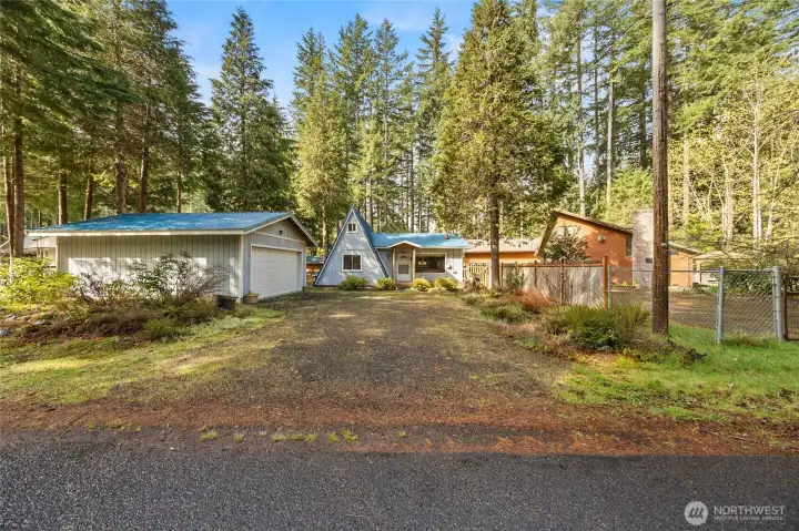 Peaceful forest setting with circular driveway, mature evergreens, and spacious detached shop/garage.