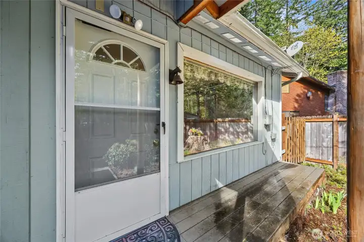 Inviting covered front porch entry with large picture window and serene woodland views.