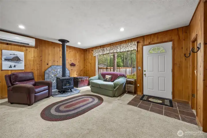 Cozy living room featuring warm wood paneling, freestanding wood stove, and abundant natural light.