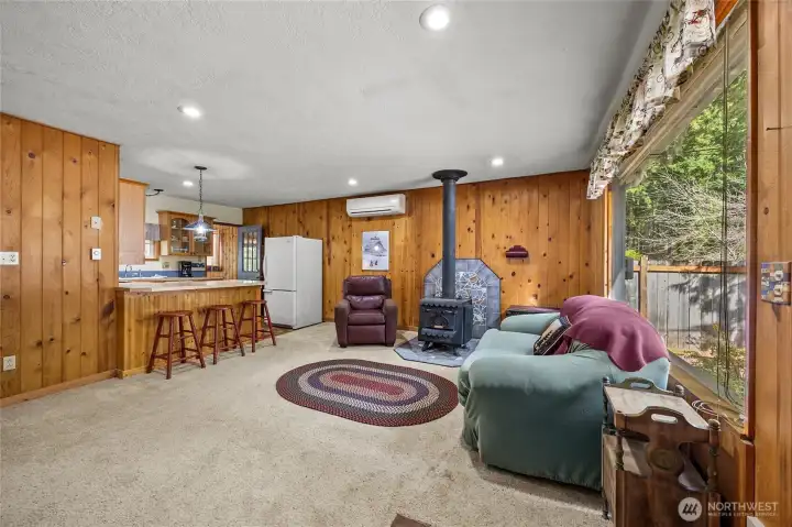 Open-concept living space with wood stove centerpiece flowing seamlessly into the kitchen area.
